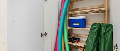 Une pièce avec une porte blanche, une étagère en bois sur laquelle se trouve une boîte de rangement bleue, et des tapis colorés.