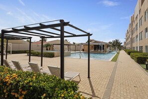 A pool area with lounge chairs and a pergola structure. - AL318 -Resort Pool-Beach Tennis court- 2BR+ condo-Close to Palm Beach (Noord)