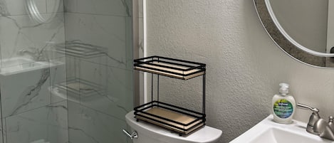 Une salle de bain avec une douche à parois de verre, des toilettes, un lavabo avec un distributeur de savon et une serviette sur le sol.