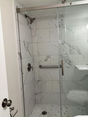 A glass-enclosed shower with a handheld showerhead, a towel bar, and a hexagonal tile floor.