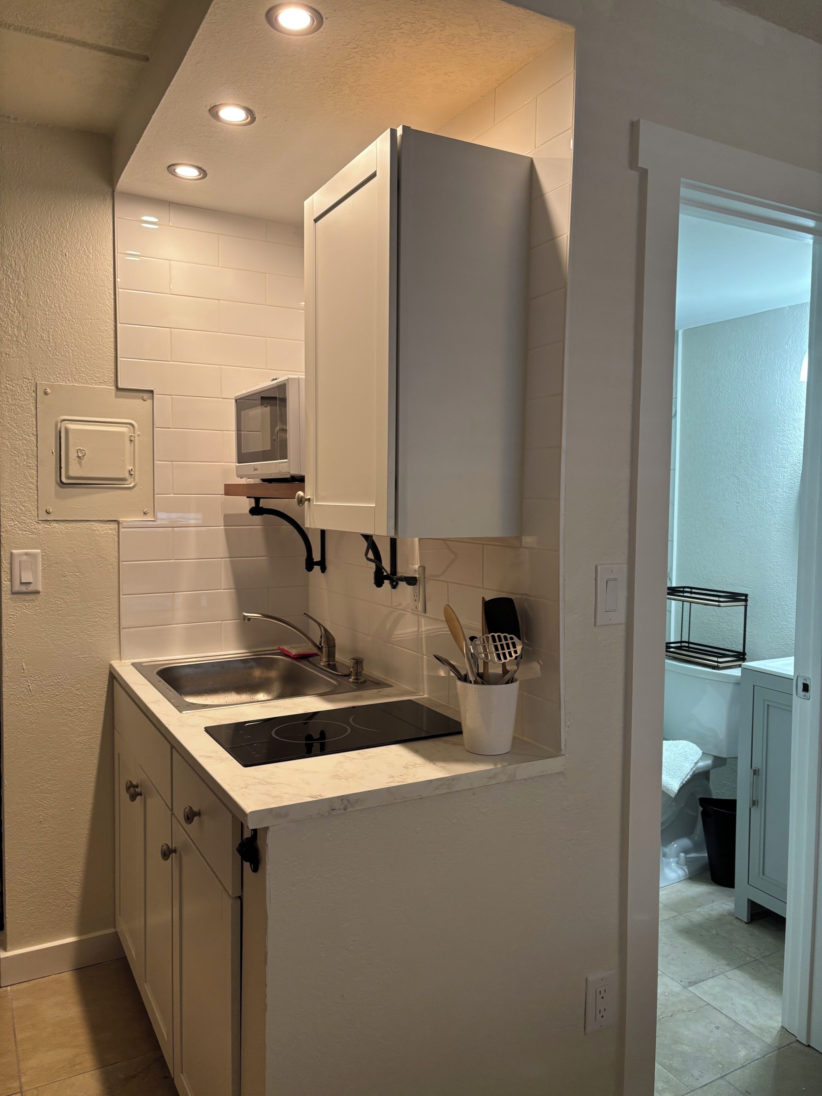 Una cocina compacta con muebles blancos, un lavamanos doble y un microondas integrado.