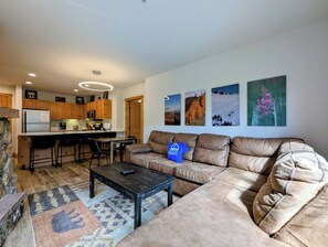 Uma sala de estar moderna com um sofá de couro, uma mesa de centro e uma área de cozinha com armários de madeira e uma geladeira.