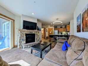 A living room with a stone fireplace, a flat-screen TV, a sofa, and a coffee table. - Stylish Mountain Retreat in the Heart of River Run. Walk to Gondola, Pool & More (Dillon)