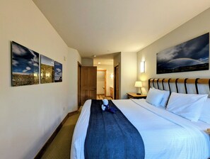 A hotel room with a large bed, a nightstand, a lamp, and a painting on the wall. - Stylish Mountain Retreat in the Heart of River Run. Walk to Gondola, Pool & More (Dillon)