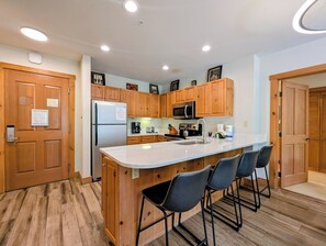 Una cocina moderna con armarios de madera, un refrigerador de acero inoxidable, un microondas y una isla grande con taburetes de bar.