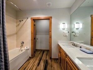 A bathroom with a wooden door, a bathtub, a shower, and a vanity with a mirror. - Stylish Mountain Retreat in the Heart of River Run. Walk to Gondola, Pool & More (Dillon)