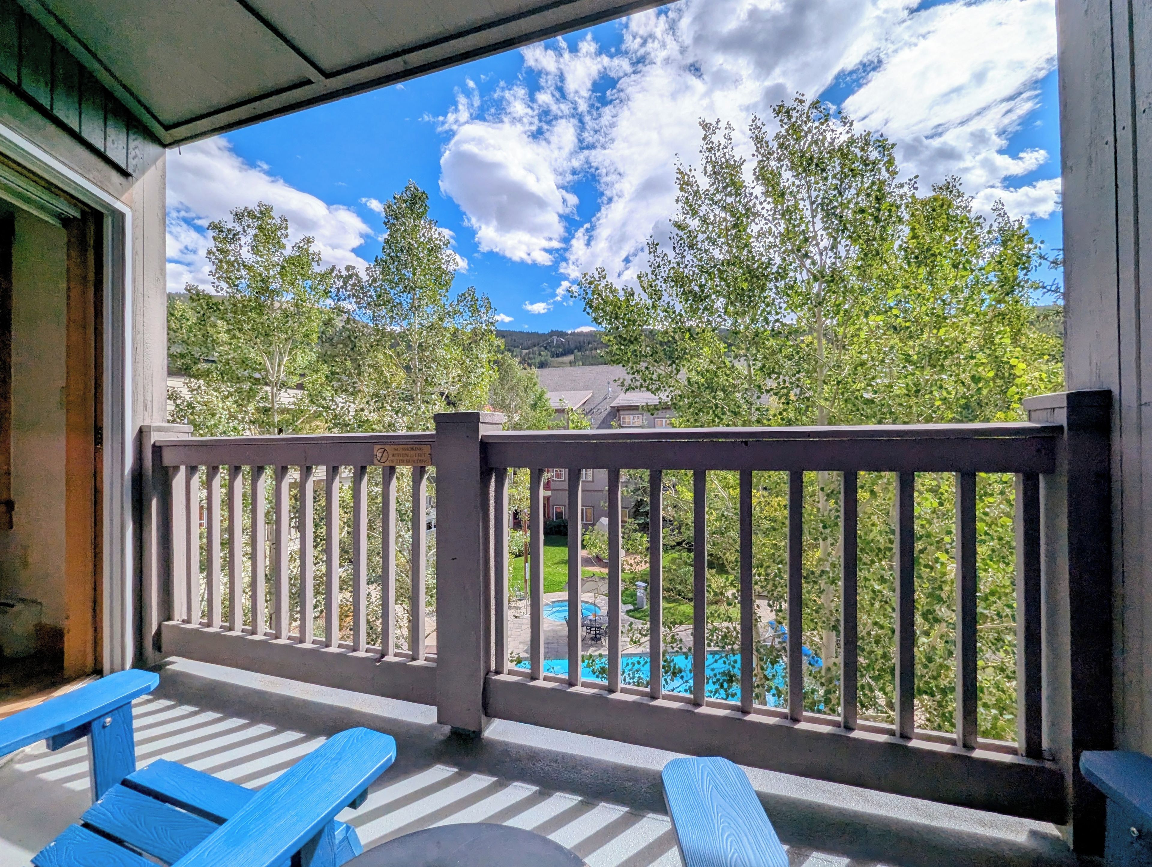 Un balcone con vista su una piscina, alberi, una recinzione in legno e una panchina.