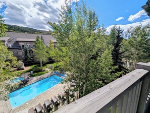A residential area with a swimming pool, lounge chairs, and a view of a forested hill. - Stylish Mountain Retreat in the Heart of River Run. Walk to Gondola, Pool & More (Dillon)
