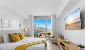 A hotel room with a bed, a desk, a chair, a TV, and a large window with a city view. - Cozy 1BR-Resort Lifestyle - Waterway View (Hallandale Beach)