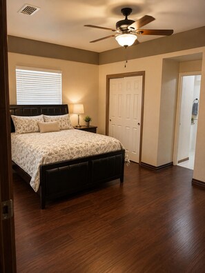 A bedroom with a bed, a ceiling fan, a nightstand with a lamp, and a door. - Rustic TX Escape in DFW, Near Stadium, Airport & Downtown (Fort Worth)