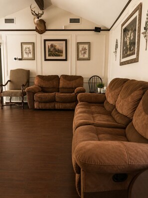 A living room with a brown leather sofa, a wooden chair, and a deer head mounted on the wall. - Spacious Getaway : 4BR-10Guest House Near AT&T Stadium, DFW Airport & Stockyards (Fort Worth)