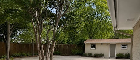 A backyard patio with a table and chairs, surrounded by potted plants and a small building.