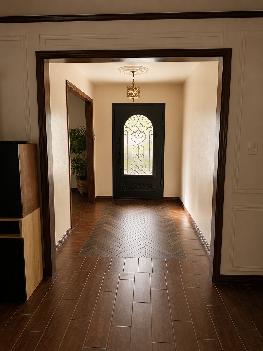 A hallway with a herringbone-patterned floor leading to a door with a decorative glass panel and a hanging light fixture.