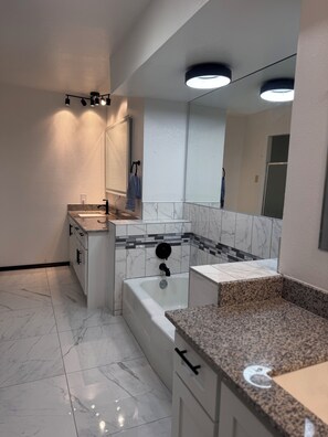A modern bathroom with a bathtub, a vanity with a sink, and a large mirror. - Rustic TX Escape in DFW, Near Stadium, Airport & Downtown (Fort Worth)