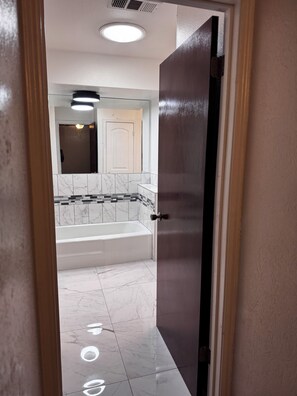 Une salle de bain avec une baignoire, un miroir et une porte donnant sur une autre pièce.