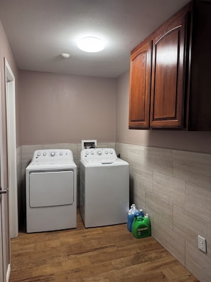 A laundry room with two front-loading washing machines, wooden cabinets, and a tiled backsplash. - Spacious Getaway : 4BR-10Guest House Near AT&T Stadium, DFW Airport & Stockyards (Fort Worth)