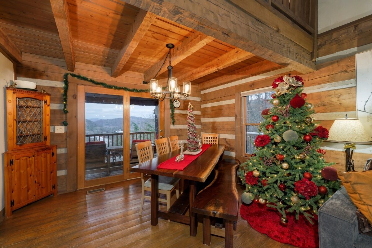 L’intérieur d’un chalet en bois, avec une table à manger, des chaises, un lustre et un sapin de Noël décoré.