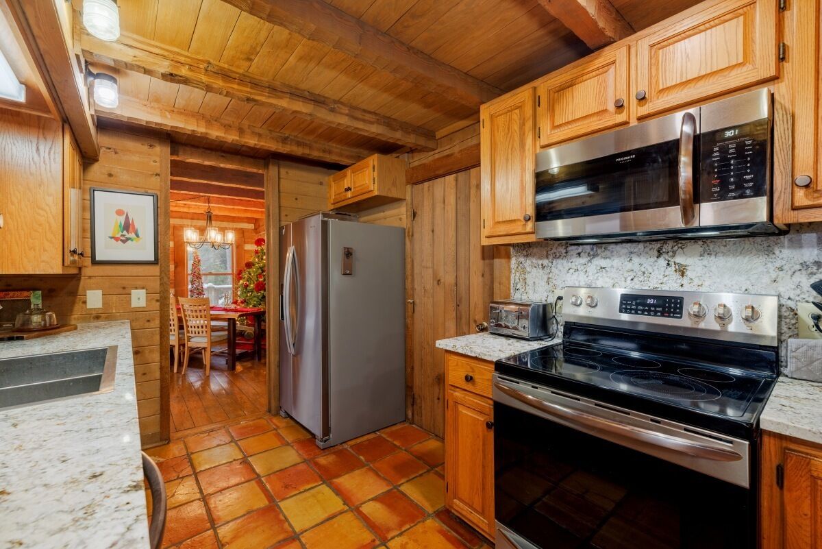 Una cocina con armarios de madera, un refrigerador de acero inoxidable, un microondas, una estufa y piso de baldosas.