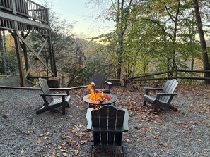 Um deck com cadeiras Adirondack, uma lareira e uma estrutura de madeira em área arborizada.