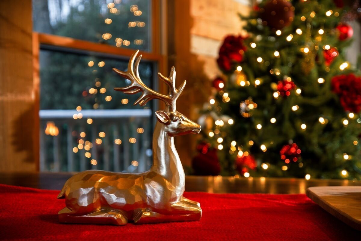 A decorative deer figurine on a red surface with a Christmas tree in the background.