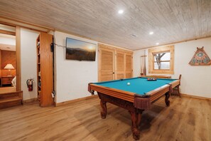A pool table in a room with wooden floors and walls, a mounted television, and a window with a view of trees. - Boone & Banner Retreat🏡.  Private Home. Hot Tub & Fire Pit. Blue Ridge views! (Banner Elk)