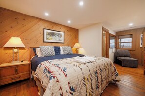 A bedroom with a wooden headboard, a bed with a patterned quilt, two bedside lamps, a framed picture on the wall, and a view through an open door. - Boone & Banner Retreat🏡.  Private Home. Hot Tub & Fire Pit. Blue Ridge views! (Banner Elk)