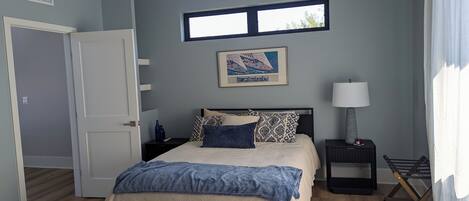 Un dormitorio con cama, mesita de noche, lámpara, ventana y puerta.