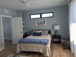Un dormitorio con cama, mesita de noche, lámpara, ventana y puerta.