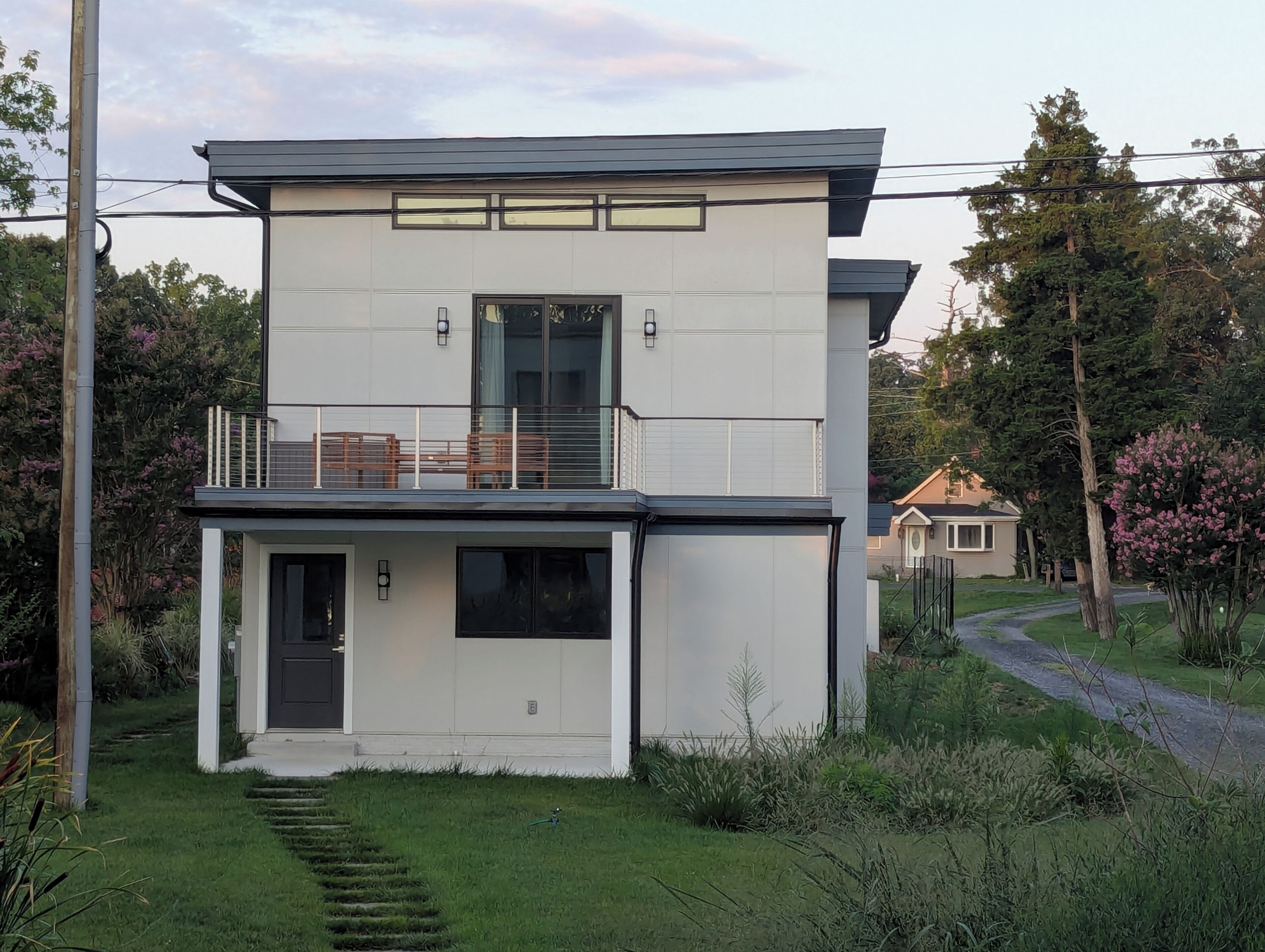 Una casa moderna de dos pisos amb un balcó, una porta d'entrada i una escala visible que condueix a l'interior.