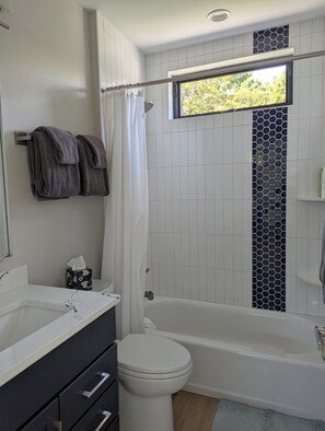 Un baño moderno con bañera, inodoro y ventana con vistas a la vegetación.