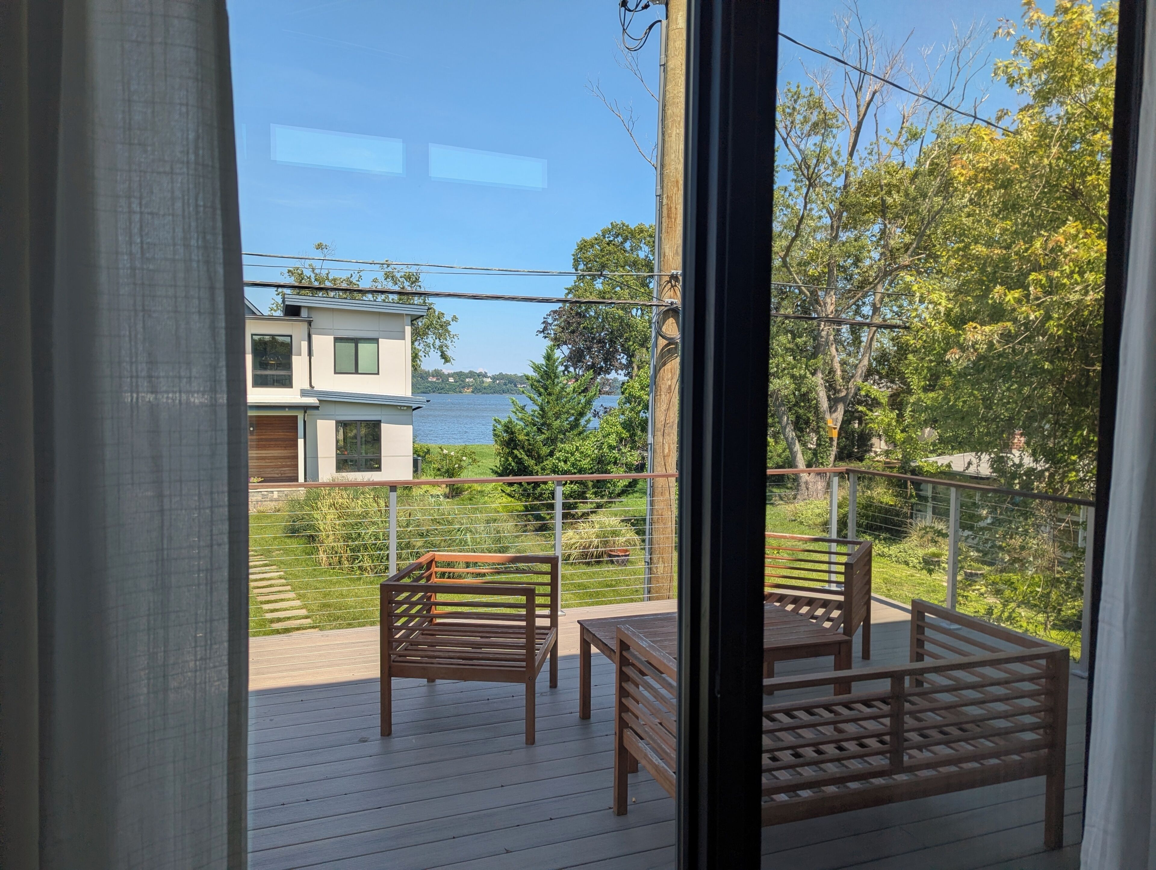 A balcony with wooden furniture, a view of a lake, and a modern building across the water.