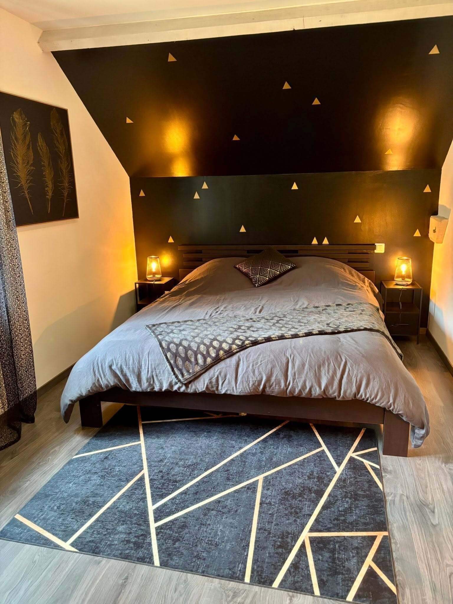 A modern bedroom with a dark headboard, two bedside lamps, a patterned rug, and a geometric floor design.