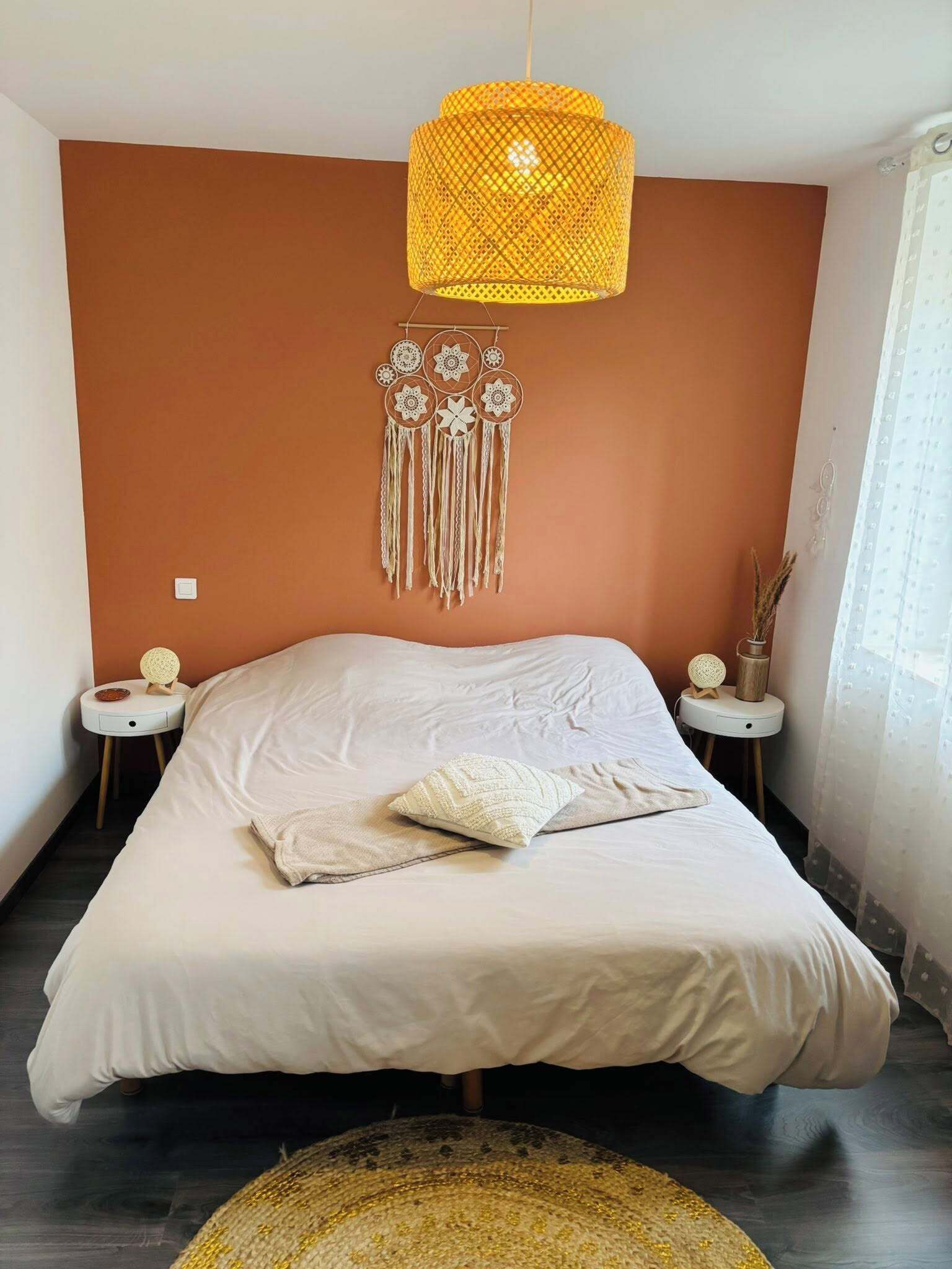 A bedroom with a large bed, a hanging light fixture, and a wall decoration.
