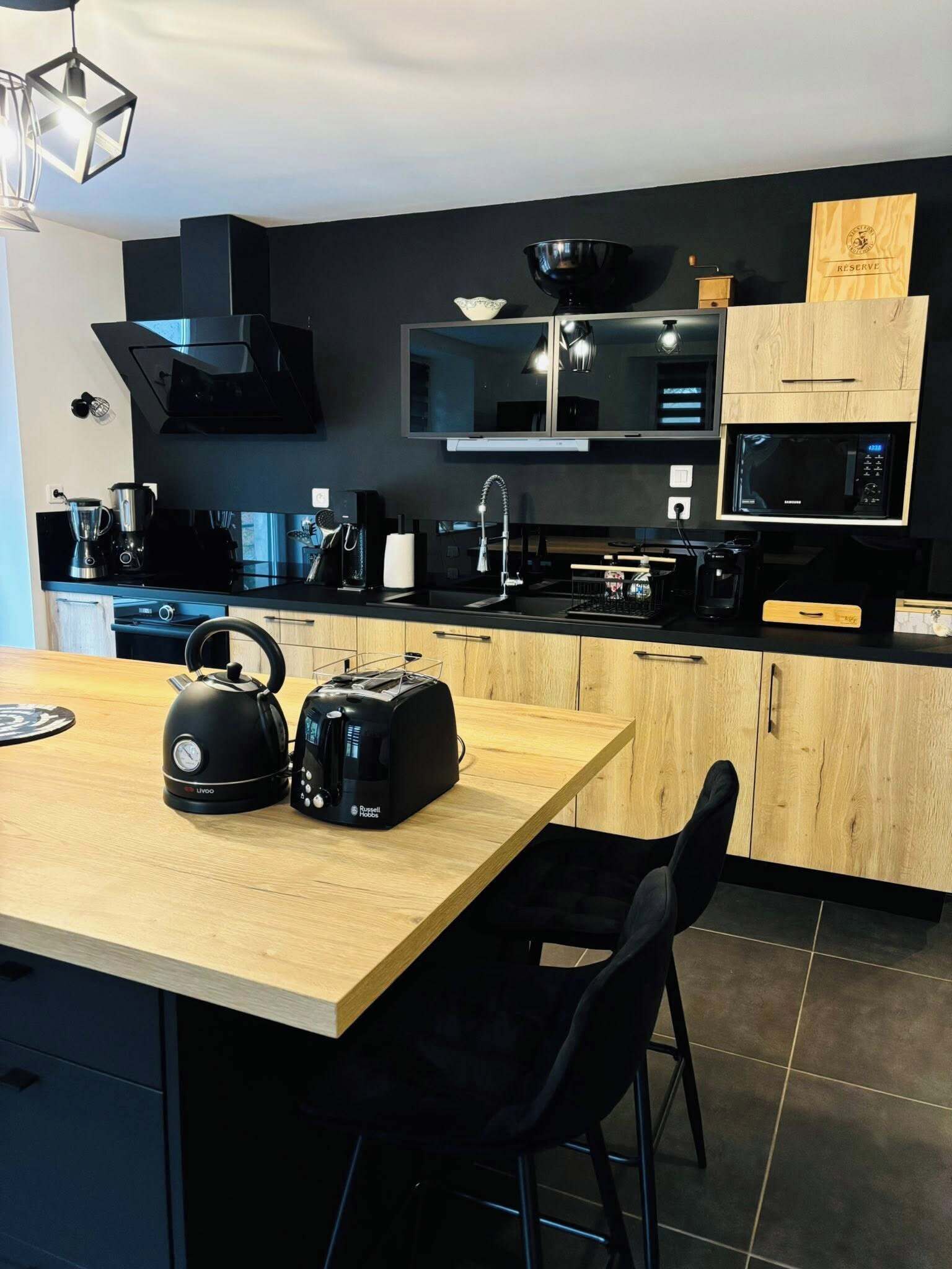 Una cocina moderna con una isla de madera, electrodomésticos negros y una pared oscura.