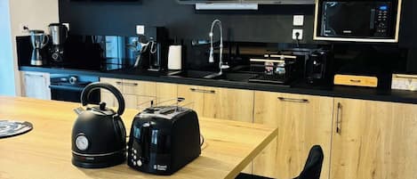 A modern kitchen with a wooden island, black appliances, and a black wall.