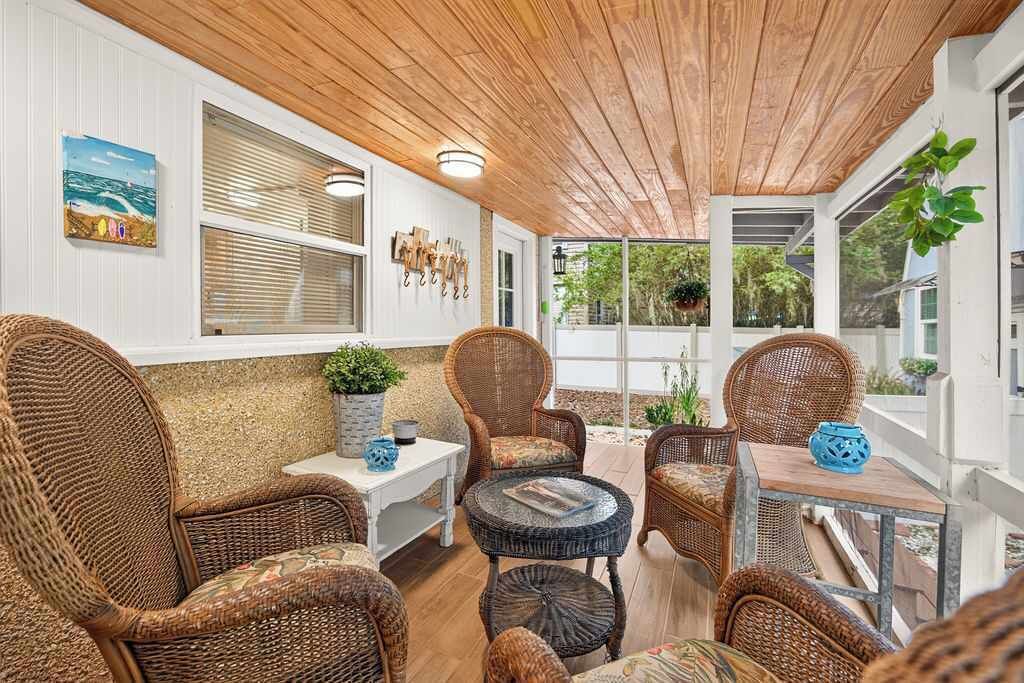 A covered outdoor seating area with wicker furniture, a small table, and a potted plant.