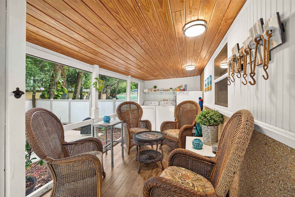 Un área de patio techada con mobiliario de mimbre, una mesa y un perchero con ganchos.