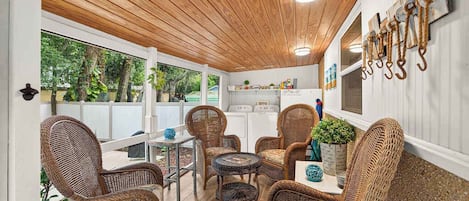 Un área de patio techada con mobiliario de mimbre, una mesa y un perchero con ganchos.