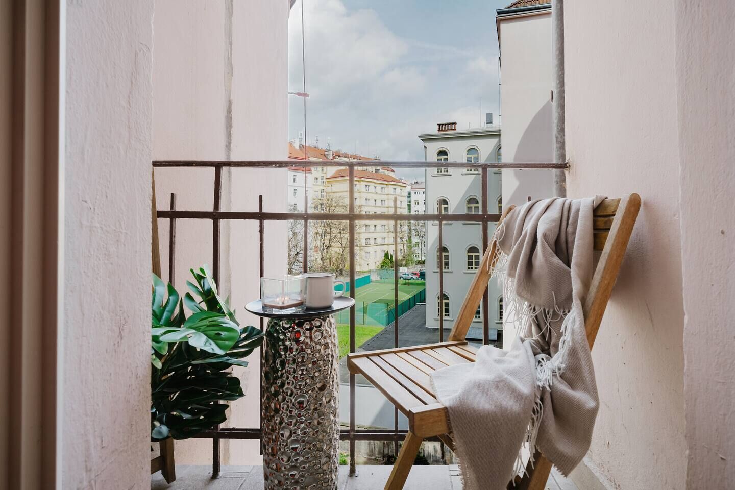 A balcony with a view of buildings, a wooden chair, a table with a candle, and a potted plant.
