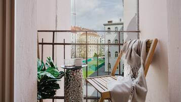 A balcony with a view of buildings, a wooden chair, a table with a candle, and a potted plant.
