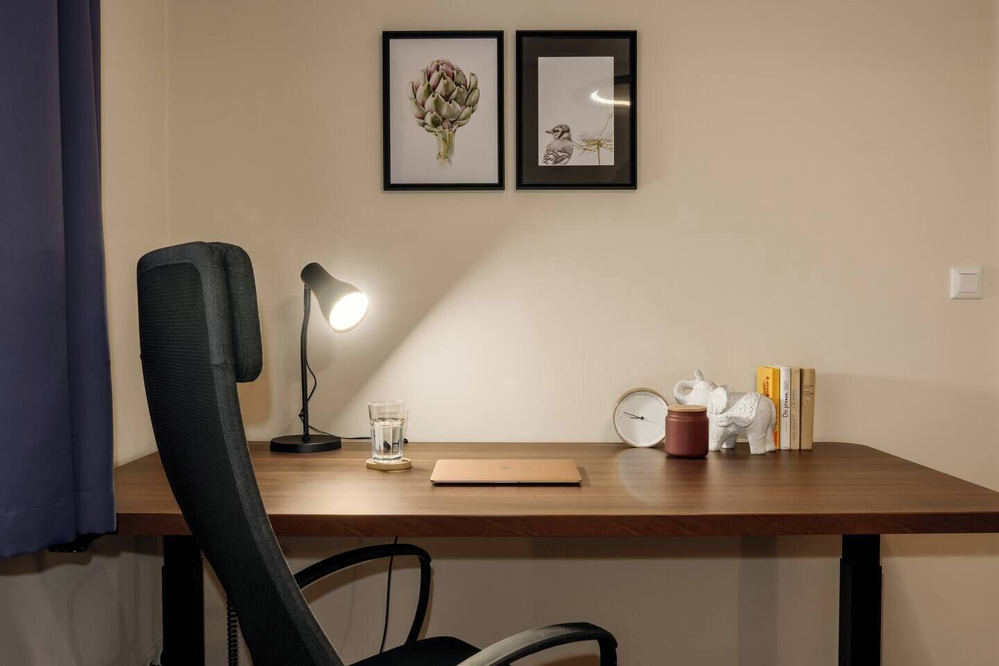A workspace with a desk, chair, lamp, glass, clock, books, and decorative items.