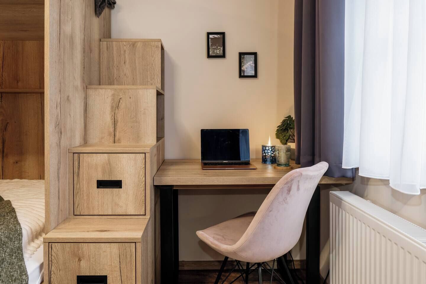 A room with a wooden desk, a laptop, a chair, and a radiator.