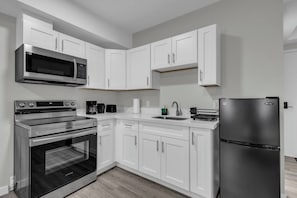 A modern kitchen with white cabinets, a stainless steel refrigerator, a built-in oven, and a microwave.