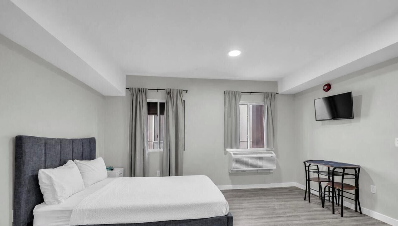 Ein Hotelzimmer mit Bett, Schreibtisch, Stuhl, Fernseher und einem Fenster mit Vorhängen.