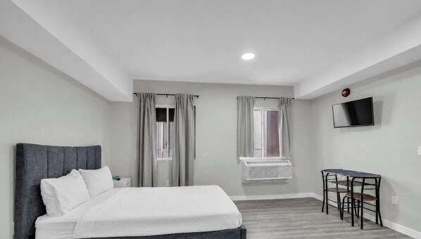 Une chambre d’hôtel avec un lit, un bureau, une chaise, une télévision et une fenêtre avec des rideaux.