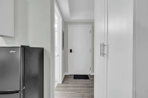 A narrow hallway with a refrigerator on the left, a door at the end, and a mat on the floor.