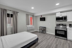 Une chambre avec un lit, une petite table et une chaise. Il y a également une kitchenette équipée d’un four à micro-ondes, d’une cuisinière et d’un four.