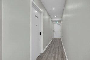 A hallway with white walls and a wooden floor, leading to a door marked 'SUITE 208'.