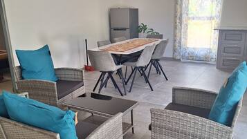 Een eetruimte met een tafel, stoelen, een koelkast en een raam met gordijnen.