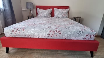 A bed with a red frame, a floral bedspread, and two pillows. There are three wall-mounted artworks above the bed.